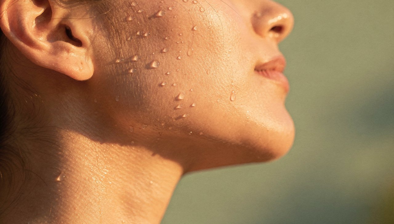 Close-up of sunlit skin with water droplets along the jawline, summer skin editorial at Facial Sculpting London