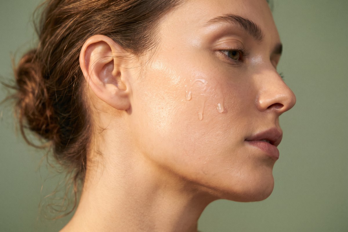 Beauty editorial close-up of a woman's glowing cheek and jawline with delicate serum droplets in soft warm light, the skin quality SkinPen microneedling builds at Facial Sculpting London